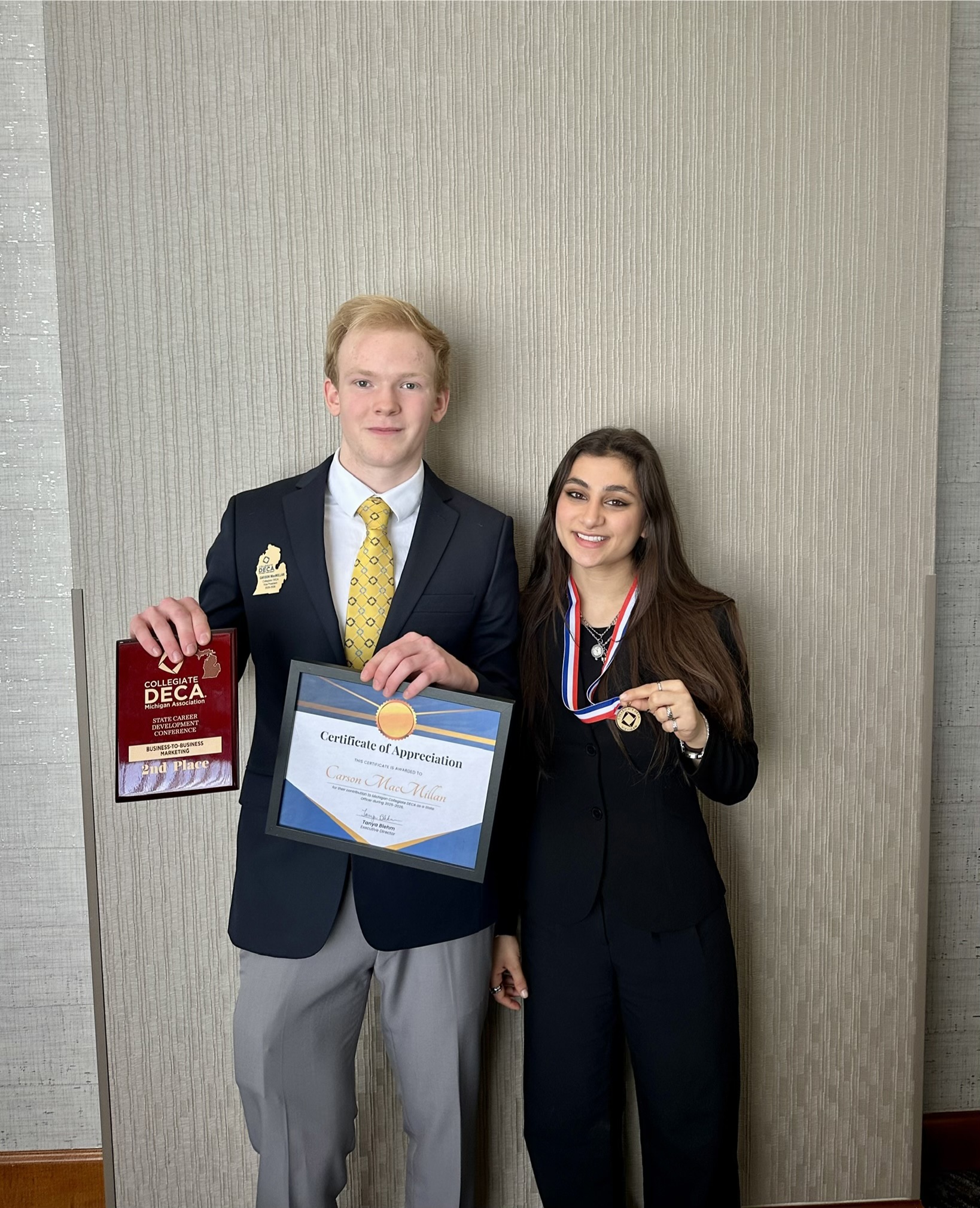 Carson MacMillan and Katie Nahhas holding awards at the Michigan Collegiate DECA conference